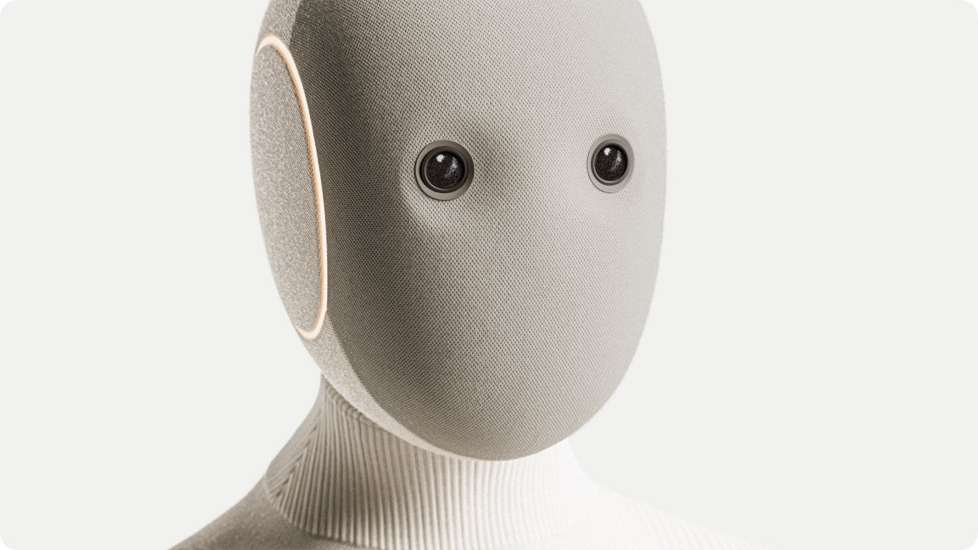 Close-up of the tan NEO robot's fabric-covered head, showing its two camera eyes and ring-shaped ear light